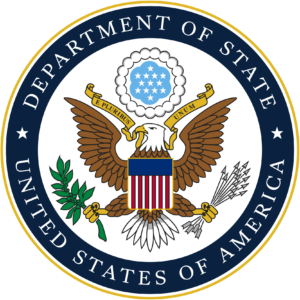 U.S. Department of State seal: eagle with blue and red and white stripe shield with an olive branch in its left claw and arrows in the right. White stars on a blue background with scalloped edge are above the head of the eagle. Dark blue border says Department of State United States of America.